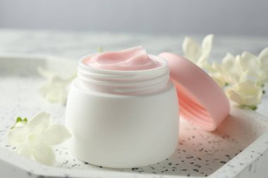 Beyaz masanın üzerinde bir kavanoz nemlendirici vücut kremi ve çiçekler, yakın plan.