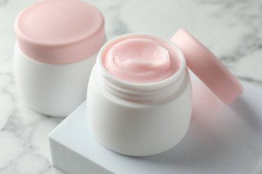 Kavanozlar dolusu nemlendirici vücut kremi beyaz mermer masada, yakın plan.