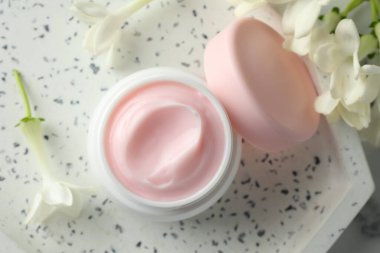 Bir kavanoz nemlendirici vücut kremi ve beyaz mermer masa üzerinde çiçekler, düz uzanmış.