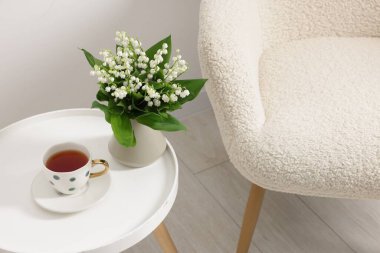 Vazodaki güzel zambak buketi ve içerideki koltuğun yanındaki kahve masasında çay.