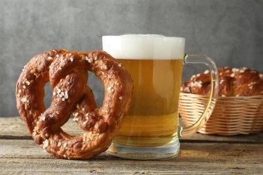 Lezzetli kraker ve bir bardak bira ahşap masada, gri arka planda, yakın planda.