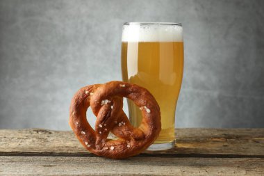 Lezzetli kraker ve bir bardak bira ahşap masada, gri arka planda, yakın planda.