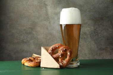 Lezzetli krakerler ve yeşil ahşap masada bir bardak bira. Gri desenli arka plan, yakın plan.