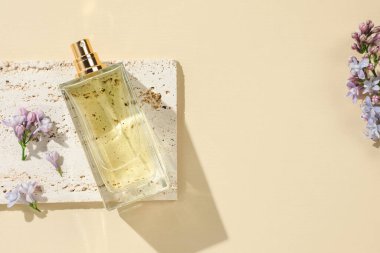 Bir şişe parfüm ve soluk sarı arka planda güzel leylak çiçekleri. Metin için boşluk