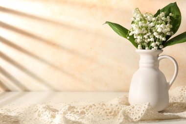 Vadi çiçeklerinin güzel zambakları vazonun içinde bej duvarın yanındaki beyaz masada. Metin için boşluk