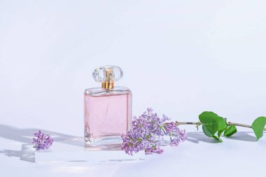 Bir şişe parfüm ve açık gri arka planda leylak çiçekleri, yakın plan.