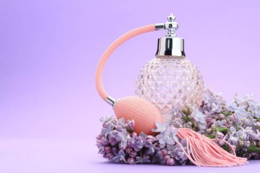 Parfüm şişesi ve mor arkaplanda leylak çiçekleri, yakın plan. Metin için boşluk