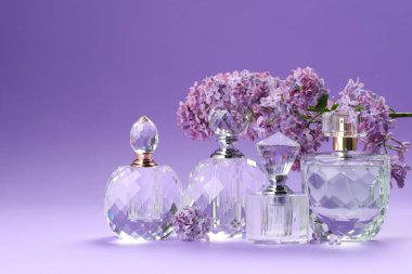 Parfüm şişeleri ve mor arkaplanda leylak çiçekleri olan dallar, yakın plan.