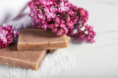 Sabun çubukları, deniz tuzu ve leylak çiçekleri beyaz mermer masada, yakın plan.