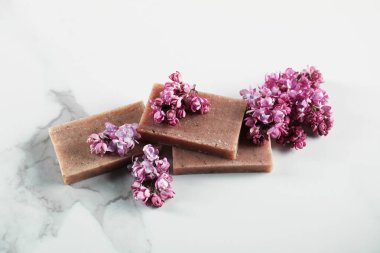 Beyaz mermer masada sabun çubukları ve leylak çiçekleri.