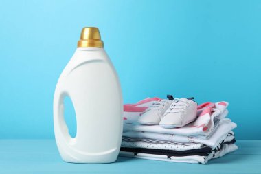 Şişe yumuşatıcı, bebek kıyafetleri ve açık mavi ahşap masa üzerindeki ayakkabılar.