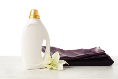 Bir şişe yumuşatıcı, üst üste yığılmış giysiler ve çiçek beyaz arka plana karşı ahşap masa