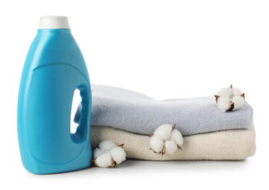 Bir şişe yumuşatıcı, üst üste yığılmış giysiler ve beyaz üzerine izole edilmiş pamuk çiçekleri.