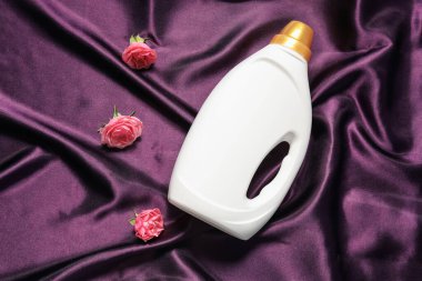 Bir şişe yumuşatıcı ve mor kumaş üzerinde çiçekler.