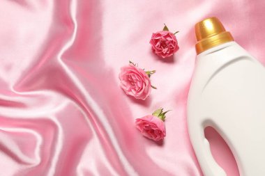 Bir şişe yumuşatıcı ve pembe kumaş üzerinde çiçekler, düz yatak. Metin için boşluk