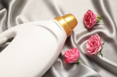 Bir şişe yumuşatıcı ve gri kumaş üzerinde çiçekler, yukarıda.