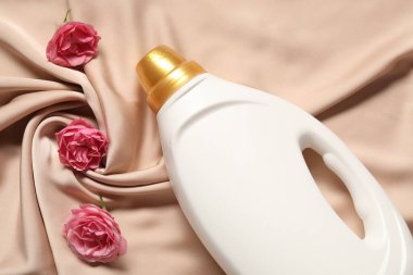 Bir şişe yumuşatıcı ve bej kumaş üzerinde çiçekler.