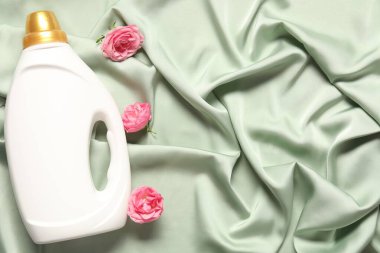 Bir şişe yumuşatıcı ve yeşil kumaş üzerinde çiçekler, düz yatak. Metin için boşluk