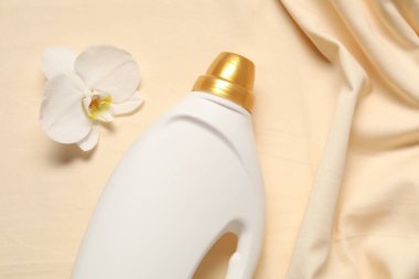 Bir şişe yumuşatıcı ve bej arka planda orkide çiçeği.