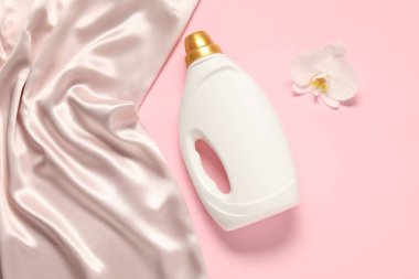 Bir şişe yumuşatıcı, orkide çiçeği ve pembe arka planda bej bez bez, düz bir zemin.