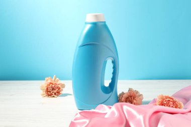 Bir şişe yumuşatıcı, temiz bez ve karanfil çiçekleri açık mavi arka planda beyaz ahşap masa üzerinde