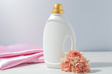 Bir şişe yumuşatıcı, temiz kıyafetler ve karanfil çiçekleri beyaz ahşap masa üzerinde.