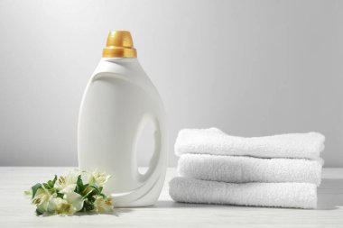 Bir şişe yumuşatıcı, havlu ve beyaz ahşap masada zambak çiçeği.