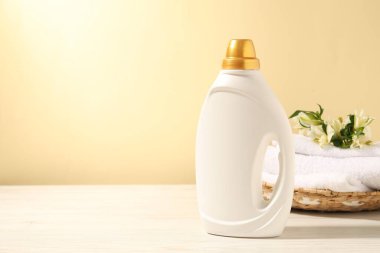 Bir şişe yumuşatıcı, terry havlular ve açık sarı arka planda beyaz ahşap masada zambak çiçekleri. Metin için boşluk