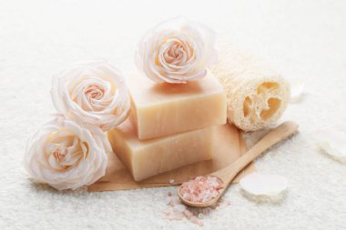 Sabun çubukları, deniz tuzu, lif süngeri ve beyaz desenli masa üzerindeki çiçekler, yakın plan.