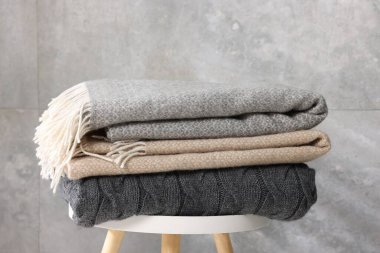 Gri duvarın yanındaki masada katlanmış yün ekose kumaşlar, yakın plan.