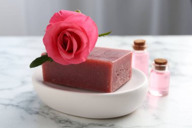 Sabun barları, kozmetik ürünleri ve beyaz mermer masada güzel bir gül.