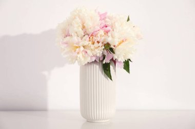 Beyaz duvarın yanındaki masada bir buket güzel şakayık.