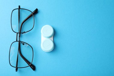 Kontak lens kutusu ve açık mavi arka planda gözlük, düz konum. Metin için boşluk