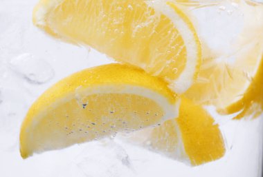 Beyaz arka planda limon dilimleri ve buzla soda tazeleniyor. Yakın plan.