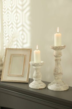 Beyaz duvarın yanındaki şöminede yanan mumlar ve diğer dekorlarla süslü şamdanlar.