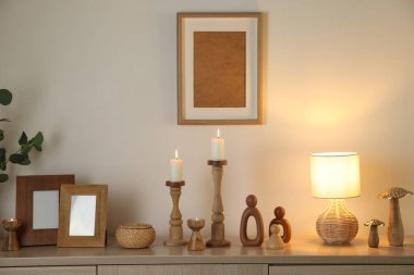 Havalı şamdanlar, yanan mumlar ve kapalı alandaki bej duvarın yanındaki dolaptaki diğer dekorlar.