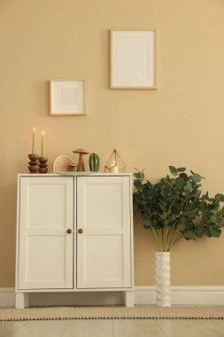 Havalı şamdanlar, yanan mumlar ve kapalı alandaki bej duvarın yanındaki dolaptaki diğer dekorlar.