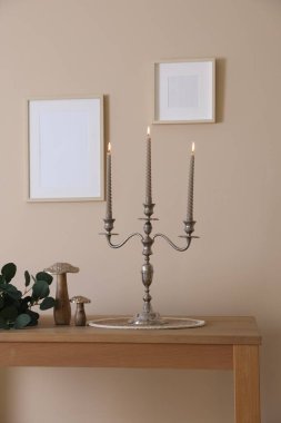 Havalı şamdanlar, yanan mumlar ve bej duvarın yanındaki ahşap masa üzerindeki diğer dekorlar.