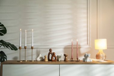 Beyaz duvarın yanındaki çekmecelerin üzerinde yanan mumlar olan şamdanlar.