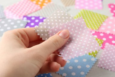 Beyaz ahşap masada farklı kumaşlardan örnekler taşıyan kadın, yakın plan.