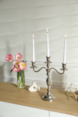 Beyaz duvarın yanındaki çekmecelerde yanan mumlar ve dekorlarla süslü zarif bir şamdan.