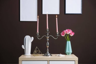 Kahverengi duvarın yanındaki dolapta yanan mumlar ve dekorlar olan zarif bir şamdan.