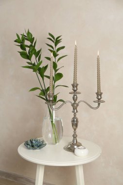 Mumları yanan zarif bir şamdan, vazoda dallar ve bej duvarın yanındaki beyaz masada diğer dekorlar.