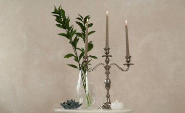 Mumları yanan zarif bir şamdan, vazoda dallar ve bej duvarın yanındaki beyaz masada diğer dekorlar.
