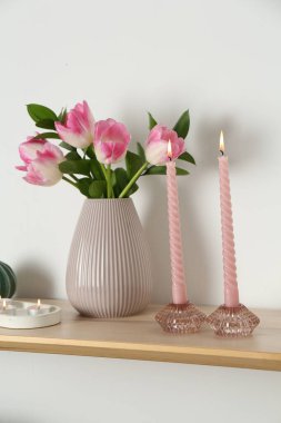 Mumları yanan zarif tutucular, vazoda laleler ve beyaz duvarın yanındaki ahşap masa üzerindeki diğer dekorlar.