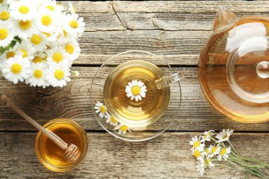 Cam bardakta nefis papatya çayı, taze çiçekler, bal ve çaydanlık ahşap masada, düz uzanmış