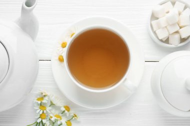 Fincanda nefis papatya çayı, taze çiçekler, şeker küpleri ve çaydanlık beyaz ahşap masada, düz uzanmış