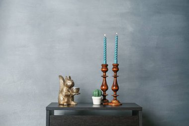 Zarif şamdanlar, yanan mumlar ve gri duvarın yanındaki siyah ahşap masa üzerindeki diğer dekorlar.