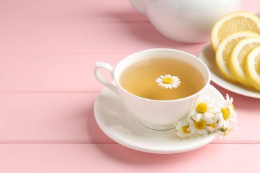 Fincanda nefis papatya çayı, taze çiçekler ve pembe ahşap masada limon, yakın plan. Metin için boşluk