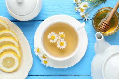 Lezzetli papatya çayı, taze çiçekler, limon ve bal açık mavi ahşap masa, düz uzanmış